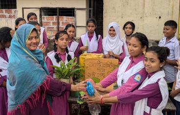 A group of South Asian girls in purple school uniforms with white sashes surrounds a project