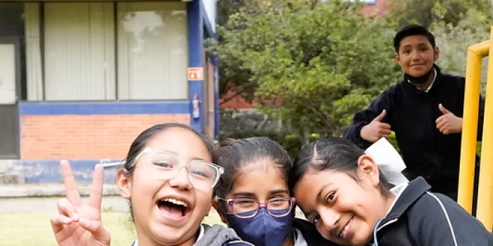 Three girls smiling at camera, a boy peaking in from behind them