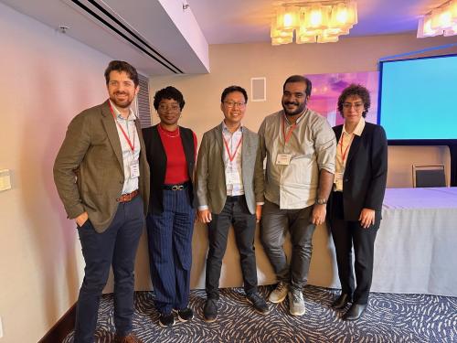 Five diverse professionals in business casual attire stand and smile for a group photo in a conference room during an educational event.