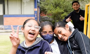 Three girls smiling at camera, a boy peaking in from behind them