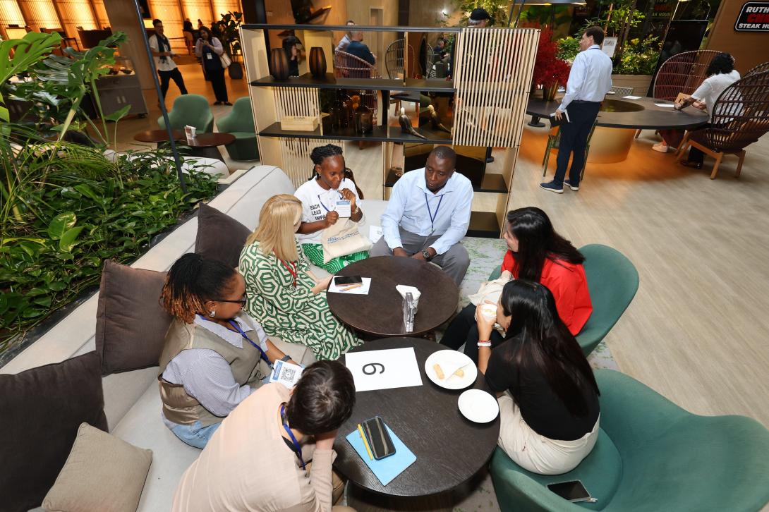 Diverse professionals gather around small tables in a modern lounge for a collaborative networking session featuring snacks, drinks, and casual discussion.