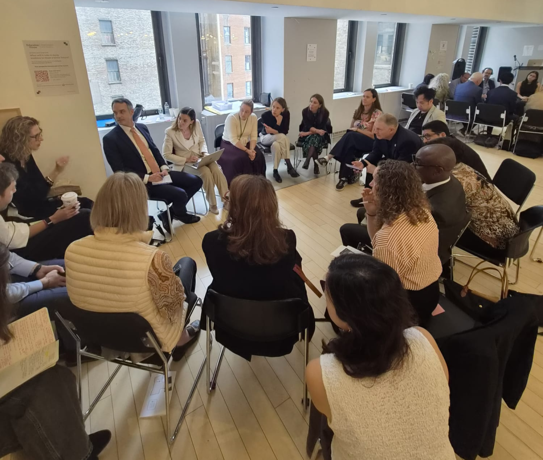 A group of diverse teachers sits in a circle of chairs inside a modern room during a discussion or workshop session.